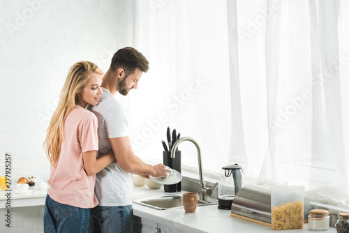 beautiful woman hugging man washing dishes at kitchen