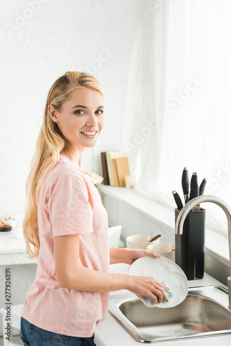 beautiful happy woman washing dishes at kitchen in morning