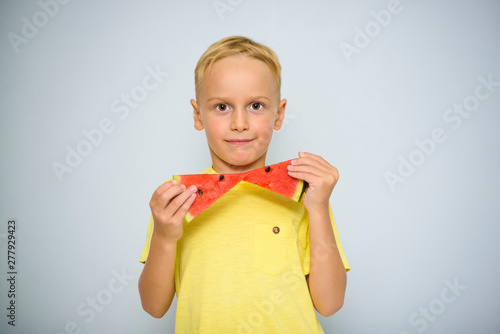 Smart caucasian 5 year old boy in yellow t-shirt holding two pieces of red watermelon as a bow tie, horizontally. photo