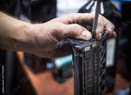 Toner refill printer cartridge. A hand is holding a screwdriver and printer cartridge.