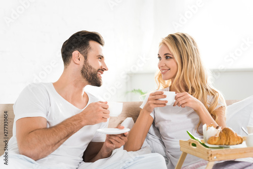 beautiful couple with cups during breakfast in bed in morning