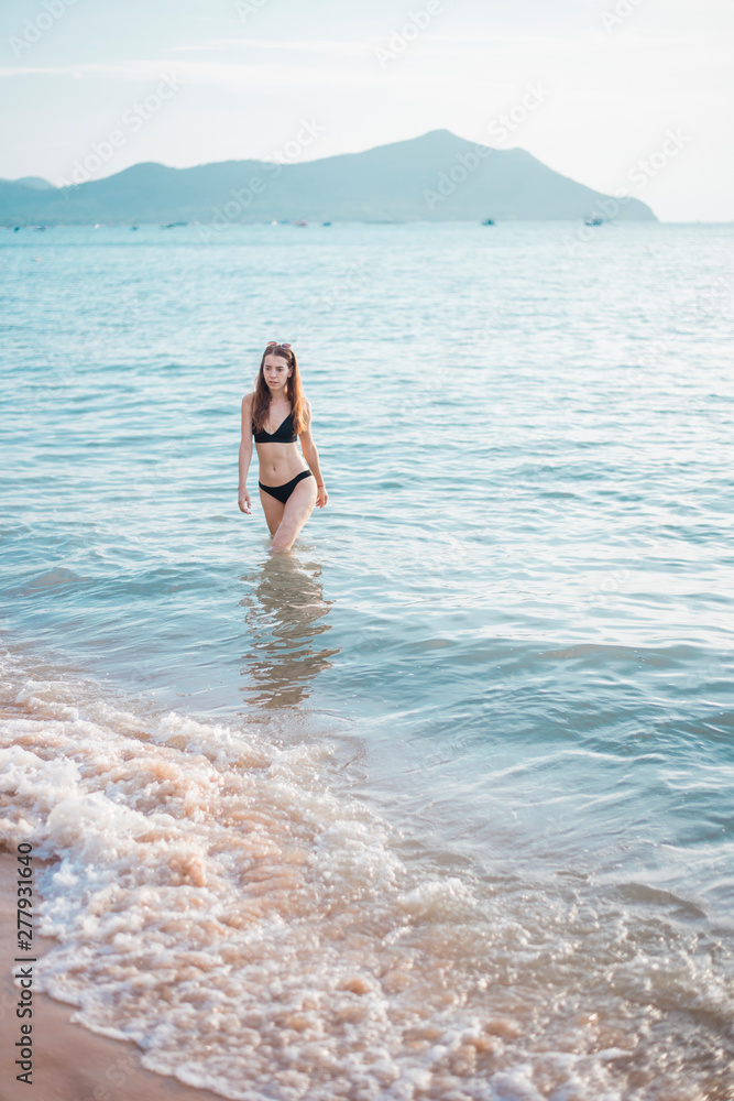 Beautiful woman in black bikini is walking from sea, summer concept