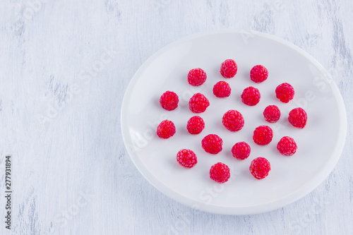 Raspberries on a white plate. Red raspberry berries on a white background. Berries for vegan. Summer concept. Minimalistic food. Top view. Copy space