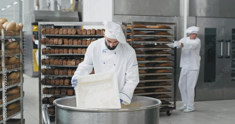 Young chef baker with a beard preparing the dough add some more flour ...