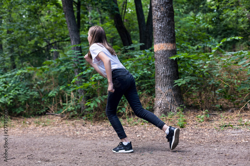 young girl in a white t-shirt in black jeans and sneakers running on the forest road