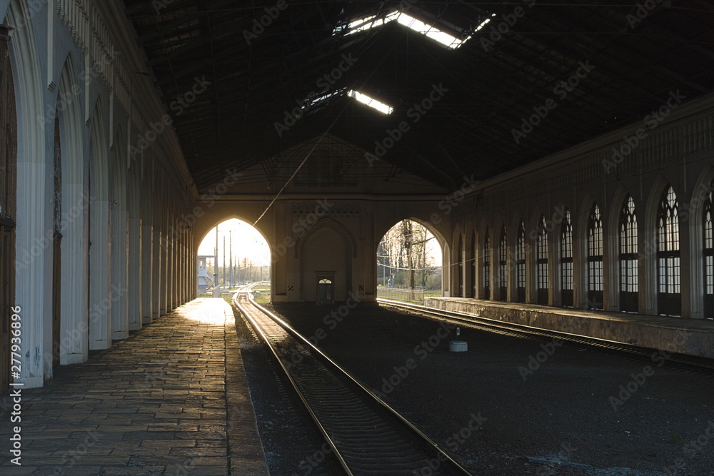 Railway tracks under the roof of the station. The light of the sun penetrates through the arches in the wall. Waiting for the train to arrive before the trip. Railway tracks under the roof of the station. The light of the sun penetrates through the arches in the wall. Waiting for the train to arrive before the trip.