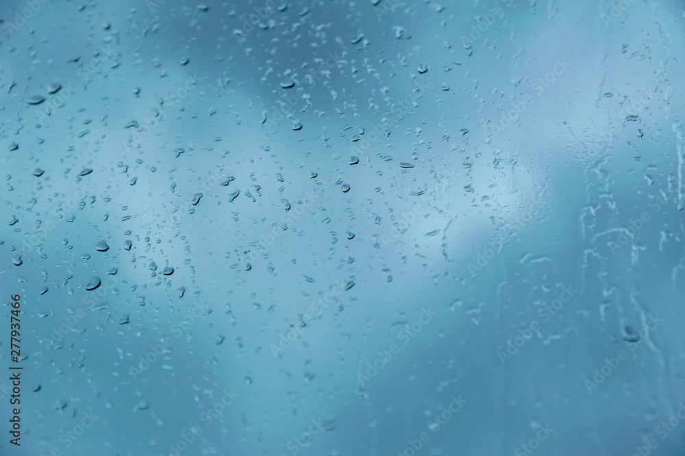 Drops of rain on the glass against the blue cloudy sky. Time before a thunderstorm. Close-up with selective focus. Abstract background Drops of rain on the glass against the blue cloudy sky. Time before a thunderstorm. Close-up with selective focus. Abstract background