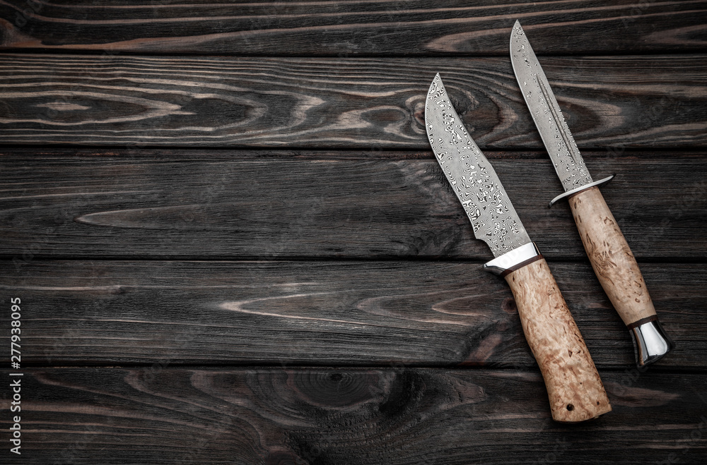 Hunting bowie knife with a wooden handle on dark wooden background. Steel arms weapon. top view Hunting bowie knife with a wooden handle on dark wooden background. Steel arms weapon. top view