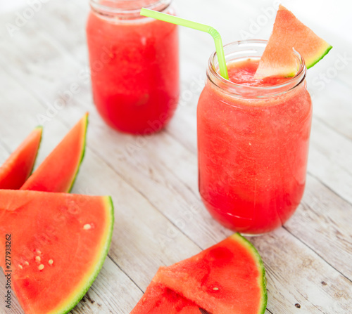 Watermelon smoothies in a glass filled with watermelon on top in a wooden background