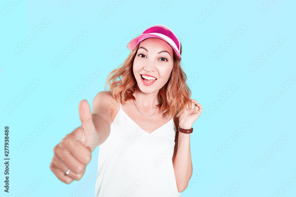 A young girl in the cap shows thumbs up on a colored background in the Studio A young girl in the cap shows thumbs up on a colored background in the Studio