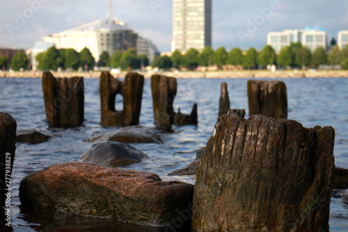 Wallpaper Mural city landscape with a river and stony shore, wooden pillars, such as letters, on a bright sunny summer day, a combination of nature and technological progress Torontodigital.ca