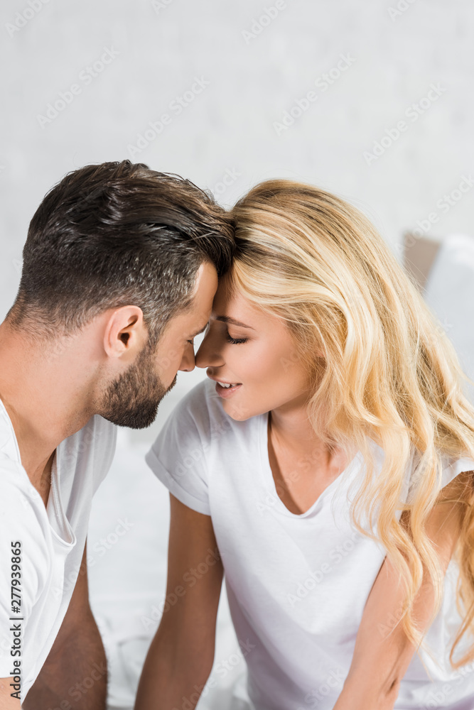 beautiful couple in white t-shirts touching with foreheads at home