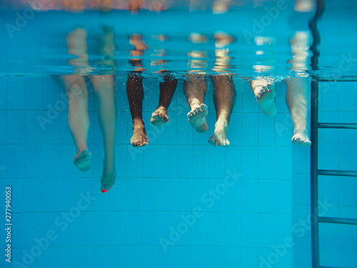 four people legs underwater in the swimming pool. Party. Summer. Vacation, diversity, friendship and sport concept. photo