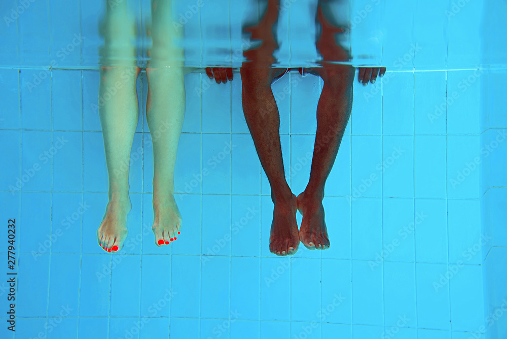 Φωτογραφία adult African American man's legs and caucasian woman legs underwater in swimming pool