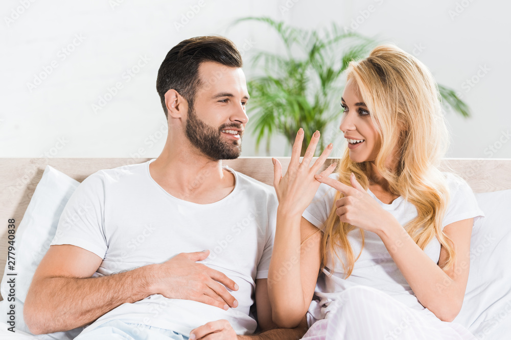beautiful woman in bed pointing at ring finger near man at home beautiful woman in bed pointing at ring finger near man at home