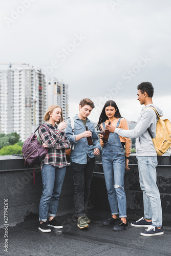 happy teenagers clinking, talking and smoking cigarette on roof