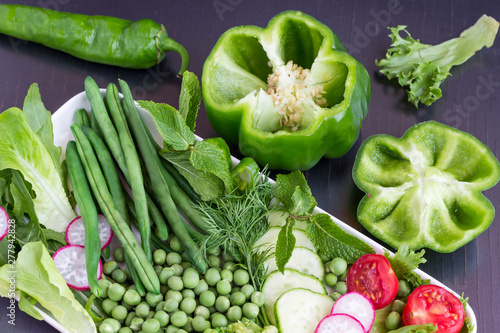 A set of vegetables: peas, green pepper, radishes, cucumber. Black background.