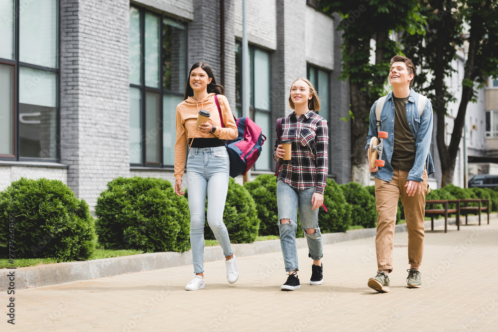 Fototapeta premium smiling teenagers walking, holding disposable cups, looking away