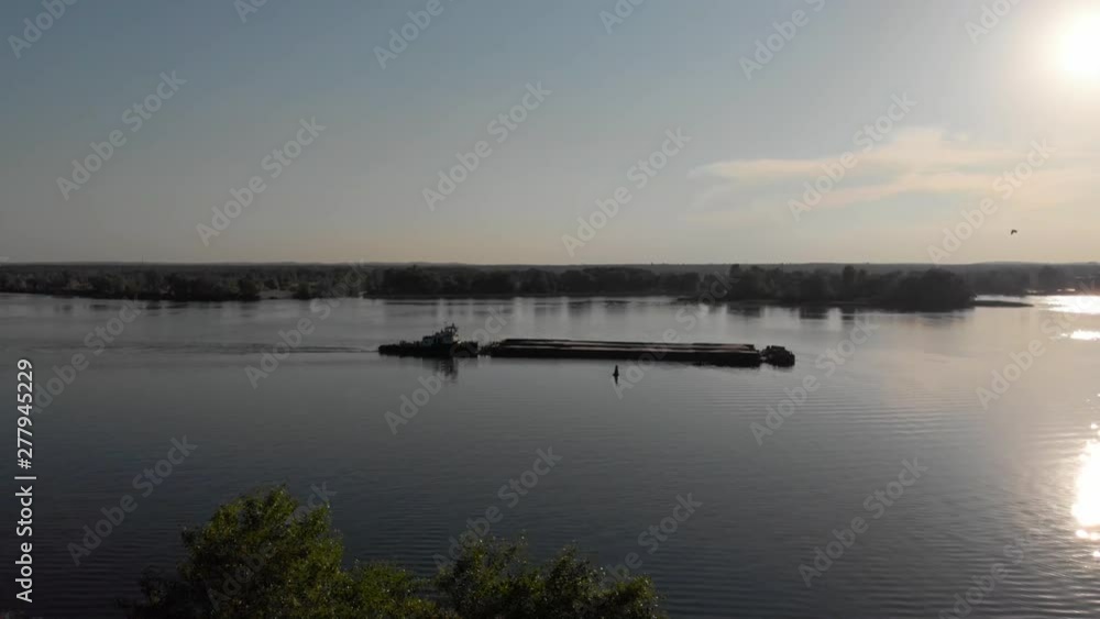 Barge ship towing sand cargo on large river with sun reflection in water Barge ship towing sand cargo on large river with sun reflection in water