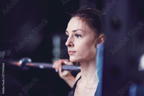 Portrait of young woman looking ahead with barbell at fitness centre photo