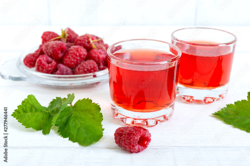 Raspberry liqueur in glass and fresh berries on a white background. Alcoholic flavored drink. Raspberry liqueur in glass and fresh berries on a white background. Alcoholic flavored drink.