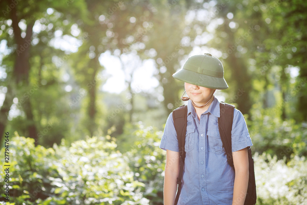 Portrait of little explorer in forest. Boy traveler in helmet play in the park. Happy child go hiking with backpack in summer nature. Dream concept.