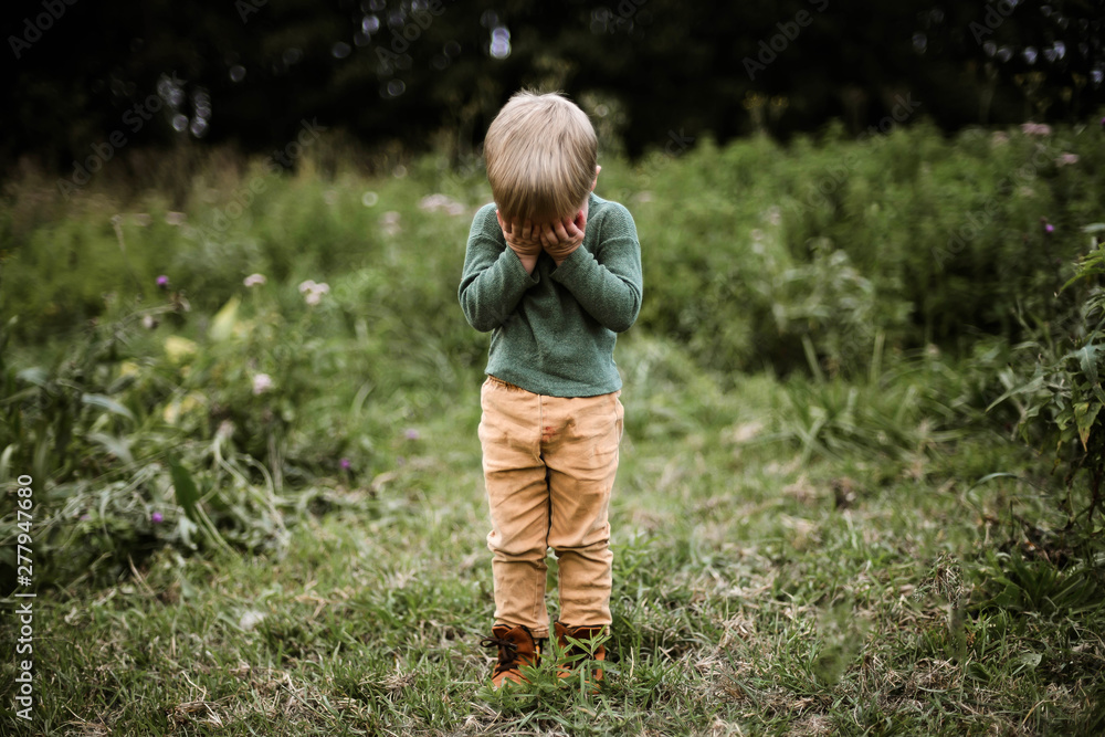 Little adorable boy covers his eyes with his hands standing outdoor Little adorable boy covers his eyes with his hands standing outdoor