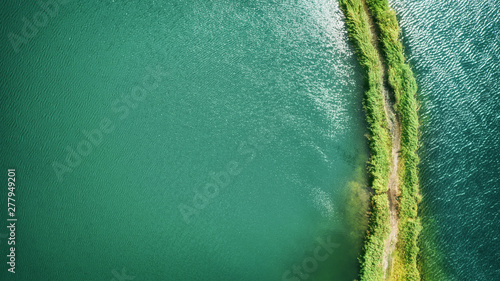 A small spit with a path covered with green grass on both sides, on a clear lake. Aerial photography photo