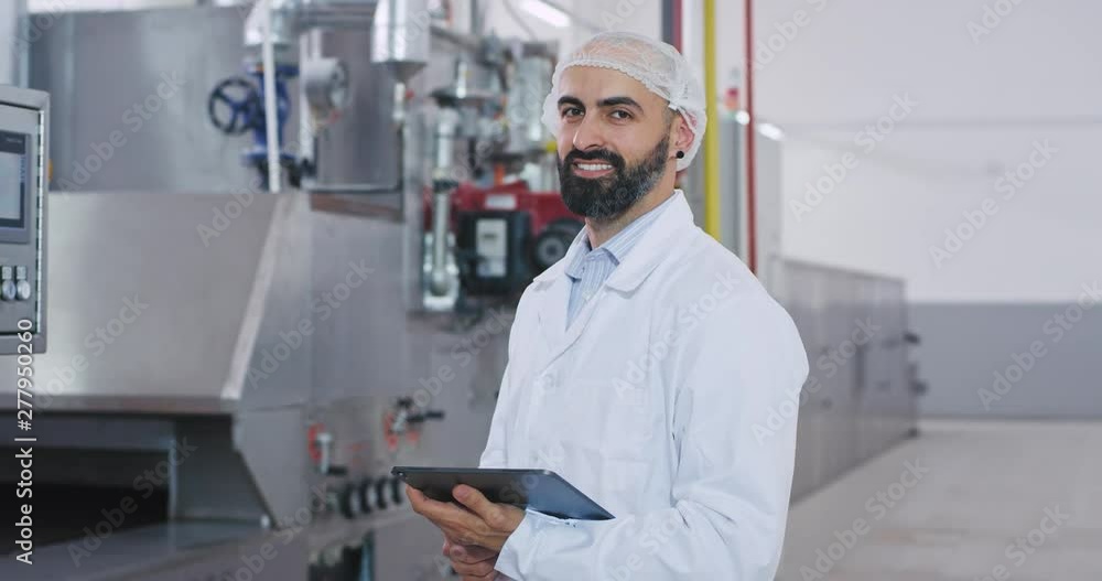 Stylish engineer man with a beard in a special white uniform monitoring the industrial machine Stylish engineer man with a beard in a special white uniform monitoring the industrial machine