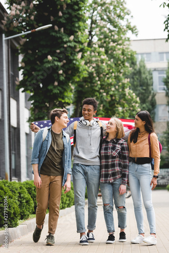 smiling and happy teenagers holding american flag and talking
