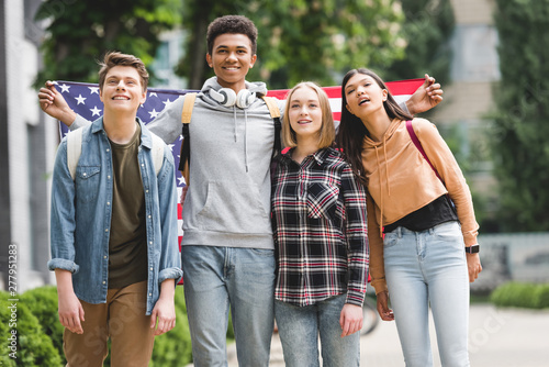 Fototapeta Naklejka Na Ścianę i Meble -  happy teenagers holding american flag, smiling and looking away