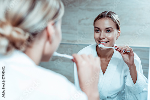 Smiling blonde lady cleaning her teeth with toothpaste