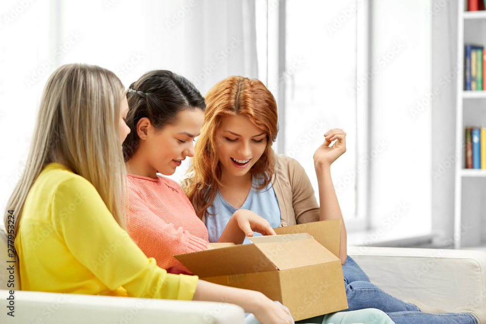 delivery and friendship concept - three teenage girls or friends opening parcel box at home delivery and friendship concept - three teenage girls or friends opening parcel box at home