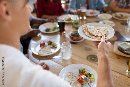 leisure, food and people concept - group of happy international friends eating at restaurant and male hand holding plate with chapati bread