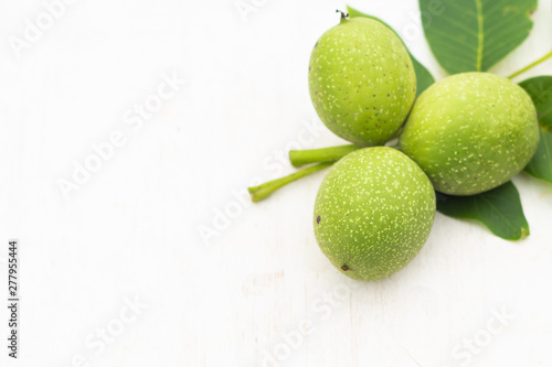 three Young green walnuts with leaves isolated on white and green background. Vegetarian food.