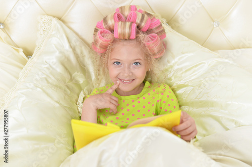 Lovely little girl with pink curlers reading