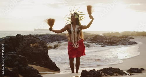Beautiful polynesian woman performing a Tahitian hula dance on the beach in slow motion at sunset with the ocean moving in the background