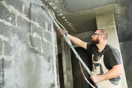 Plasterer using screeder spraying putty plaster mortar on wall photo