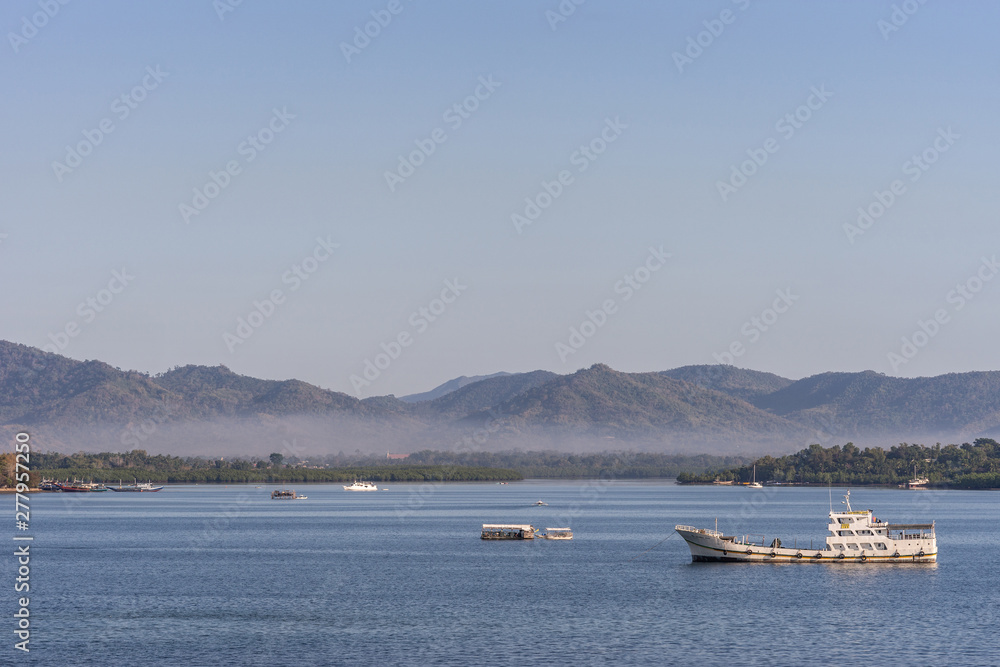 Puerto Princesa, Palawan, Philippines - March 3, 2019: The bay in front of the city shows blue water and brown mountains coverd in a light haze in the distance. Few boats. Light blue sky.