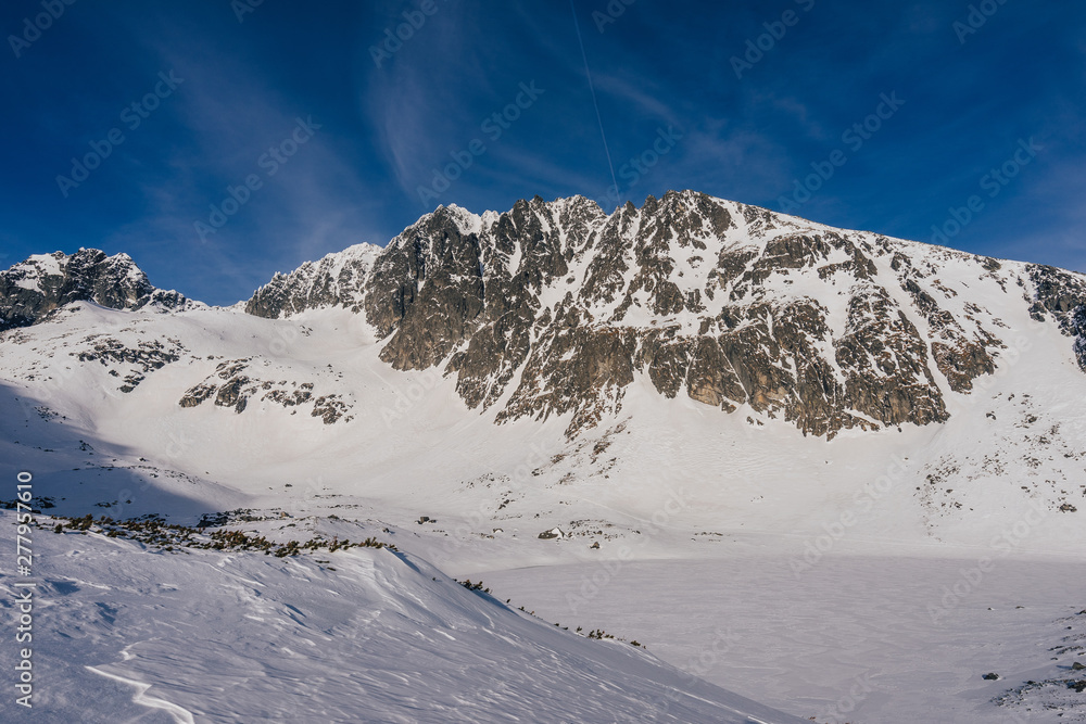 Obraz premium Winter view of the highest mountain of Slovakia and High Tatras, Gerlach mountain. Gerlachovsky stit in winter. High alpine mountain landscape covered with snow and ice. Blue vibrant sky.