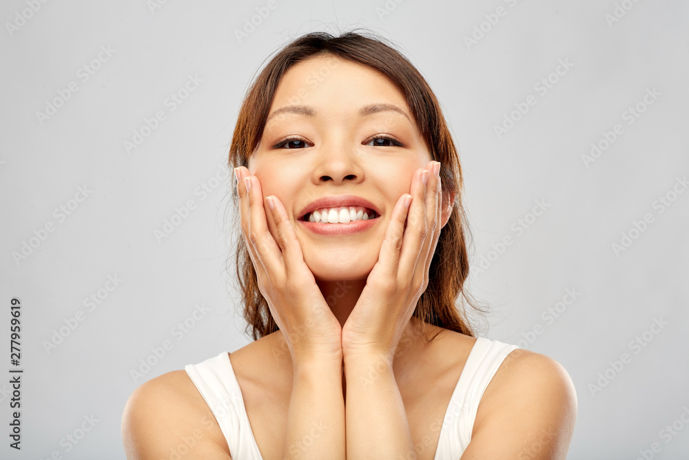 beauty and people concept - happy smiling young asian woman touching her face beauty and people concept - happy smiling young asian woman touching her face