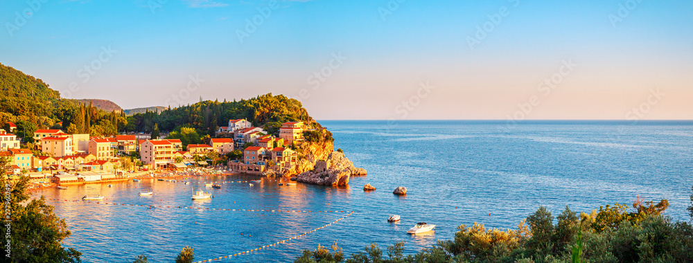 Picturesque summer view of Adriatic sea coast in Budva Riviera. Przno village with buildings on the rock at sunset warm sunlight, Montenegro - obrazy, fototapety, plakaty 