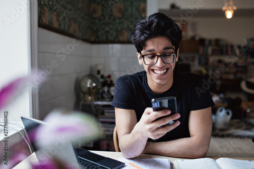 Smiling young man using smartphone at home
