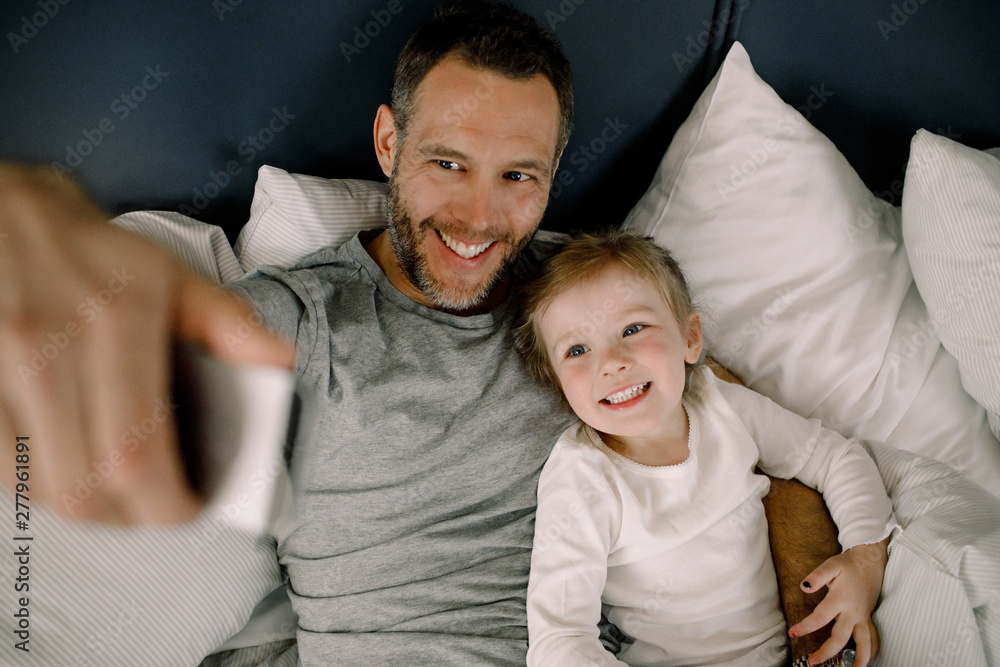 High angle view of happy father taking selfie with smiling daughter on bed in hotel High angle view of happy father taking selfie with smiling daughter on bed in hotel