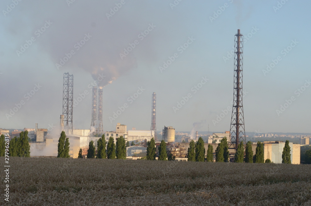 Factory pipes pollute the air on the background of a wheat field. Pollution of the environment. Factory pipes pollute the air on the background of a wheat field. Pollution of the environment.