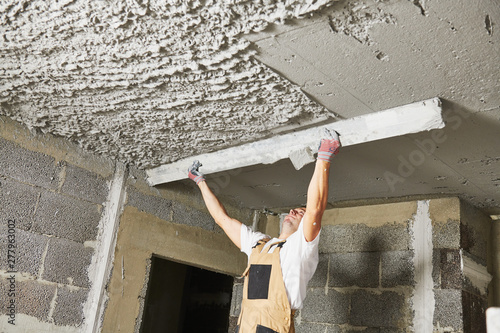 Plasterer smoothing plaster mortar on ceiling with screeder photo
