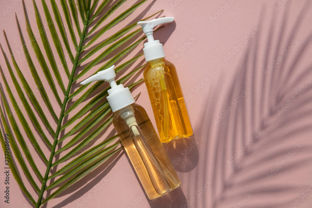 Fototapeta premium Natural cosmetic oil in a clear bottle with tropical leaf and shadow