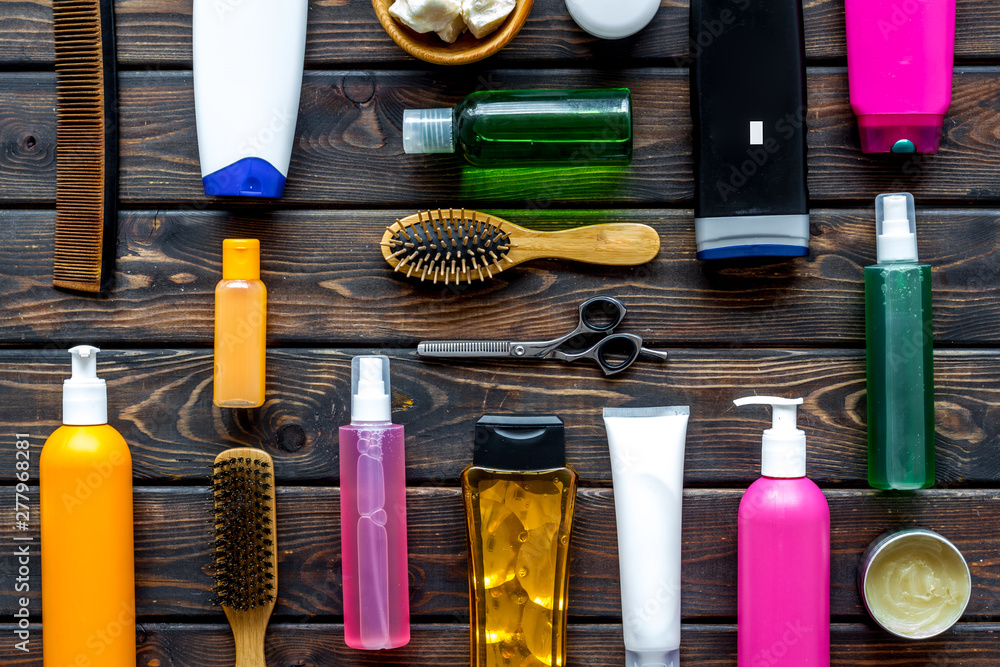 Fototapeta premium Cosmetics for hair with oil, scissors, comb, conditioner and shampoo in bottle on wooden background top view pattern