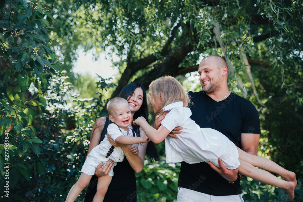 couple of brother and sister in white clothes play with a dad and mom in the park or garden couple of brother and sister in white clothes play with a dad and mom in the park or garden