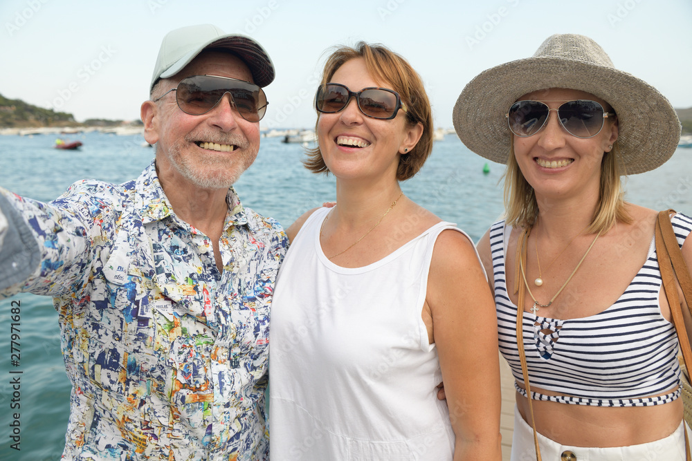 Portrait of two happy women and an older man over seaside promenade taking selfie
